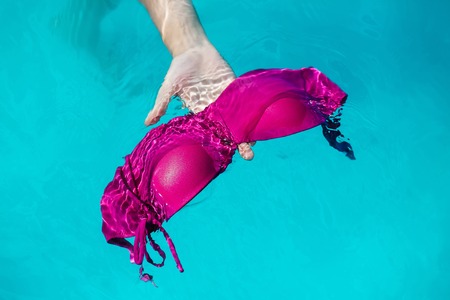 hand with wet female swimsuit bra or brassiere pink color floating in blue water of swimming pool with nobodyの写真素材