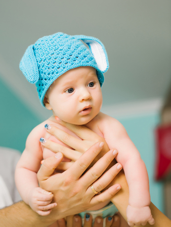 Small boy kid with adorable curious surprised face in cute funny blue bunny hat holding by fathers and mothers parent handsの写真素材