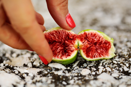 Female fingers with fig fruit with red juicy flesh and green skin cut in at halves on grey backgroundの写真素材