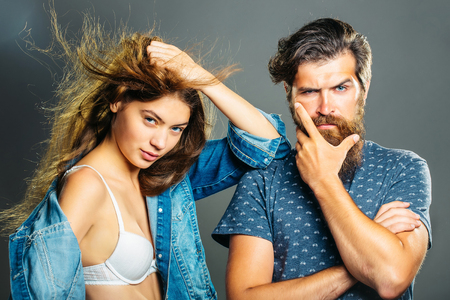 Fashion couple of pretty girl in bra denim jacket and handsome bearded man hipster pose on grey backgroundの写真素材
