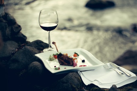 Picnic near water, decorated meat with lemon, glass of wine, served foodの写真素材