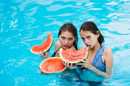 young sexy women or girls with pretty face and wet hair swimming in pool with blue water eating red watermelon sunny summer day outdoorの写真素材