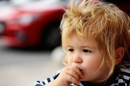 Cute baby boy child with curly blond hair and brown eyes in striped shirt outdoors on summer dayの写真素材