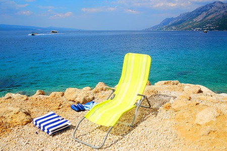 Yellow beach chair empty chaise lounge on rocky shore on sunny summer day on beautiful blue sea and skyの写真素材