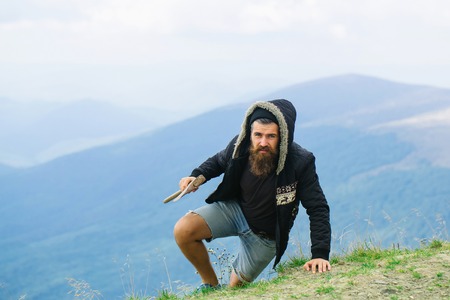 Strong man lumberjack hipster with long beard and moustache in coat and hood with axe in hand on...