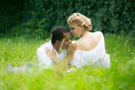 Romantic couple of man handsome african American and pretty girl embrace on green grass on summer dayの写真素材