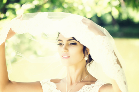 sexy bride woman with pretty face under wedding veil on sunny summer day outdoor on blurred backgroundの写真素材