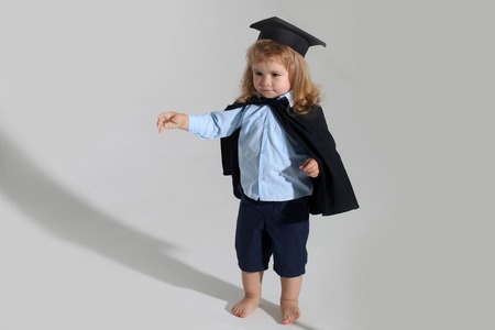Small boy child with long blond hair in blue shirt black graduation gown and cap isolated on white backgroundの写真素材