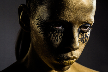 sexy golden woman or girl has pretty face with makeup and body art metallized color and black eyes, closeupの写真素材