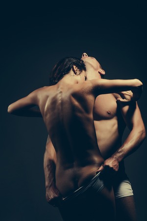 young couple of pretty slim sporty woman with long curly hair and sexy buttocks and handsome muscular man with fit body topless in panties on studio backgroundの写真素材