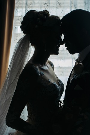 Silhouette of bride beautiful young woman and groom handsome african American man share love head to head on background of windowの写真素材