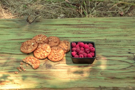 Harvesting bunch of fresh organic ripe raspberries in bowl and tasty cakes with peanuts on wooden board background outdoorの写真素材