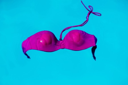 wet female swimsuit bra or brassiere pink color floating in blue water of swimming pool with nobodyの写真素材