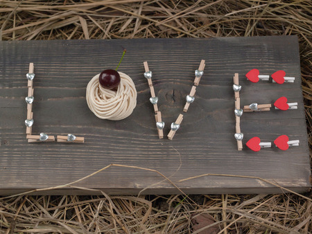 Word love writing with clothes pin red and silver hearts and cherry on wooden board on hay backgroundの写真素材