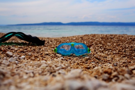Mask goggles and flipper for diving snorkeling or swimming in sea on pebble beach on summer day over blue seascapeの写真素材