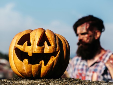 Halloween pumpkin traditional autumn holiday symbol with bearded bloody man zombie hipster on blue skyの写真素材