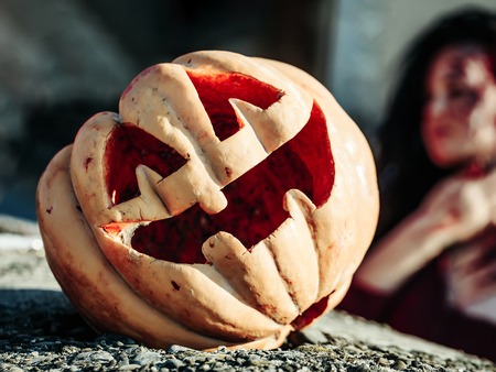 Halloween pumpkin traditional autumn holiday symbol with young bloody woman zombie girl outdoors on sunny dayの写真素材