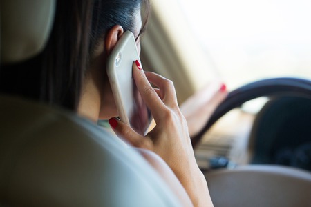 Business brunette driver woman sitting in leather salon hold steering wheel driving car and talking on cell phone concentrating on roadの写真素材