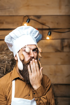 Funny man chef cook or baker with beard and moustache in hat toque with wooden spoons and hand near...