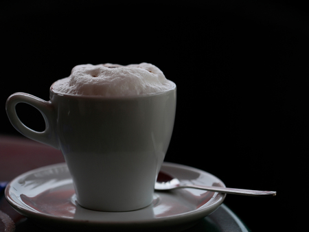 White cup of cappuccino or coffee with milk foam on saucer with tea spoon copy space on black backgroundの写真素材