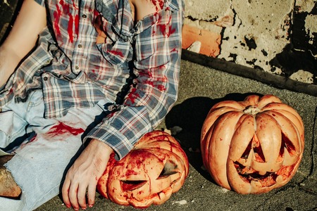 Halloween pumpkins traditional autumn holiday symbols with bloody man zombie with wounds and red blood outdoors on sunny dayの写真素材