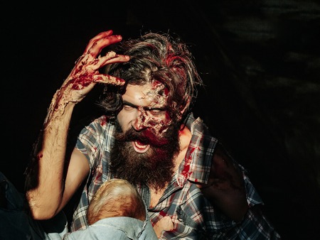 Scary zombie man with beard creepy vampire or bloody war soldier with wounds and red blood outdoors on dark backgroundの写真素材