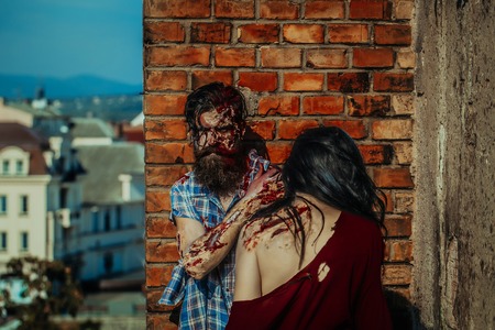 Halloween zombie couple of bearded man hipster or war soldier and bloody young woman with wounds and red blood outdoors on brick wallの写真素材