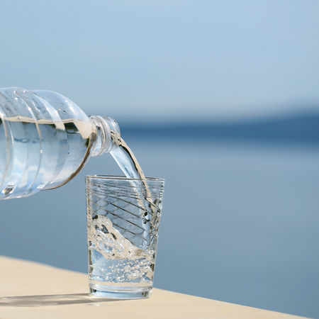 pure drinking water from plastic bottle pouring into glass outdoor on summer day on blue sea