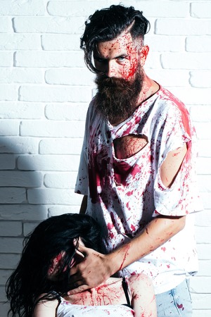 Bearded man zombie bloody hipster and creepy girl young woman with wounds and red blood on brick wallの写真素材