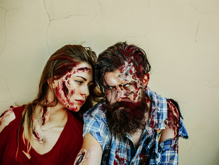 Halloween zombie couple of bearded man hipster or war soldier and bloody young woman with wounds and red blood sit on beige wallの写真素材