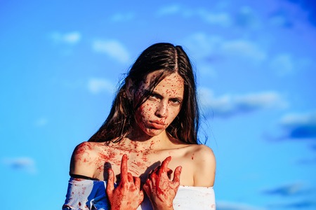 Halloween zombie girl or pretty young woman with bloody brunette hair with wounds and red blood...