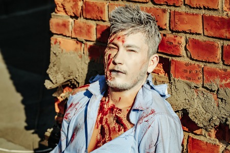 Halloween zombie man handsome young vampire or bloody war soldier with wounds and red blood outdoors...