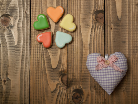 Beautiful heart pillow made of decorative textile symbol of valentines day and colorful tasty cookies on wooden background copy spaceの写真素材