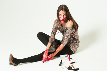 Pretty zombie girl or young woman with brunette hair with wounds and blood prepares for halloween party with makeup isolated on whiteの写真素材