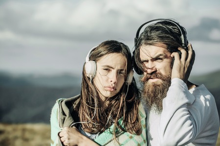 Young couple of pretty girl covered in blanket and bearded man hipster with beard listen to music with headphones on mountain sceneの写真素材
