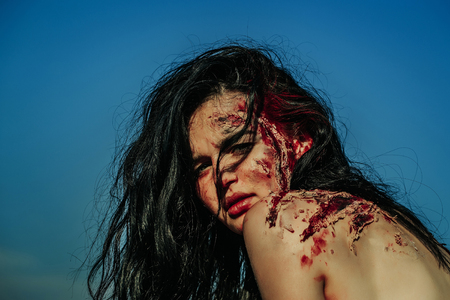 Halloween zombie girl pretty young woman with bloody brunette hair with wounds and red blood outdoors on blue skyの写真素材