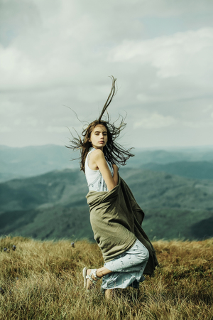 Pretty cute sexy woman or girl in blue dress and brunette hair waving in wind stay with veil on outdoor on beautiful landscape on cloudy sky backgroundの写真素材