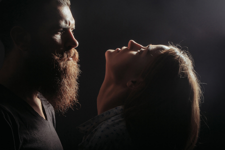 young couple silhouette of handsome bearded man with long beard and pretty sexy woman or girl with cute face and red hair in studio on black backgroundの写真素材