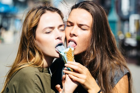 Couple of two pretty sexy cute women or girls eating ice cream outdoor on blurred background, close upの写真素材