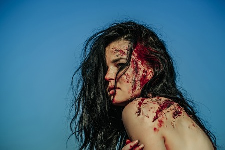 Halloween zombie girl pretty young woman with bloody brunette hair with wounds and red blood outdoors on blue skyの写真素材