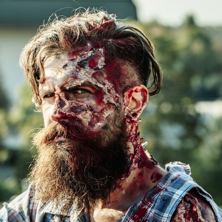 Bearded zombie man with beard halloween vampire or bloody war soldier with wounds and red blood outdoors on natural backgroundの写真素材