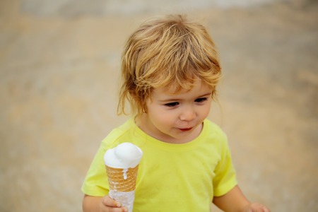 Cute baby boy child with curly blond curly hair in yellow shirt with ice cream outdoor on blurred...