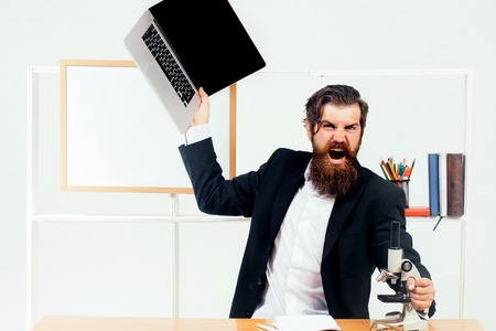 Angry man businessman male scientist hipster with laptop and microscope shouts furiously in office with board for copy space on white backgroundの写真素材