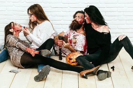 Zombie people of bearded man with beard and three girls young bloody women with pumpkin and axe ready for halloween on wooden floorの写真素材