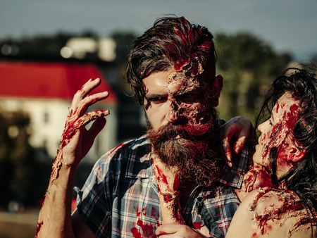 Halloween zombie couple of bearded man hipster or war soldier and bloody young woman with wounds and red blood outdoorsの写真素材