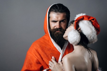 couple of bearded handsome santa claus man in new year coat and pretty sexy girl in christmas hat on grey background, copy spaceの写真素材