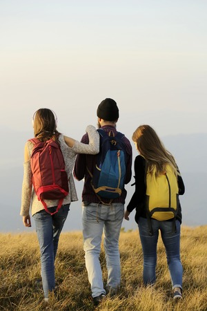 handsome man with two pretty sexy cute girls or women standing with colorful backpacks a on mountain topの写真素材
