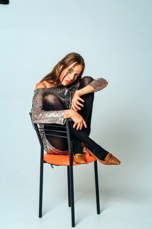 Pretty zombie girl or young woman with brunette hair with blood and bloody makeup red lips for halloween party sits on bar chair on grey backgroundの写真素材