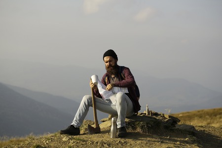 young handsome bearded hipster man in checkered shirt with long beard holding axe or ax on mountain...