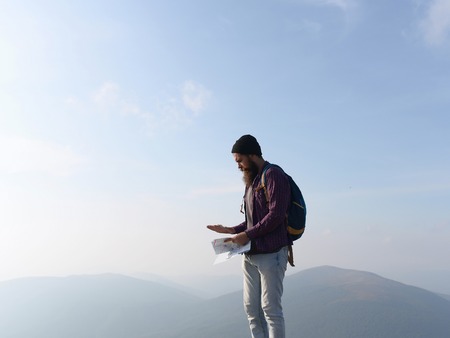 handsome bearded man with mustache and long lush beard on serious face with backpack and map on blue sky backgroundの写真素材